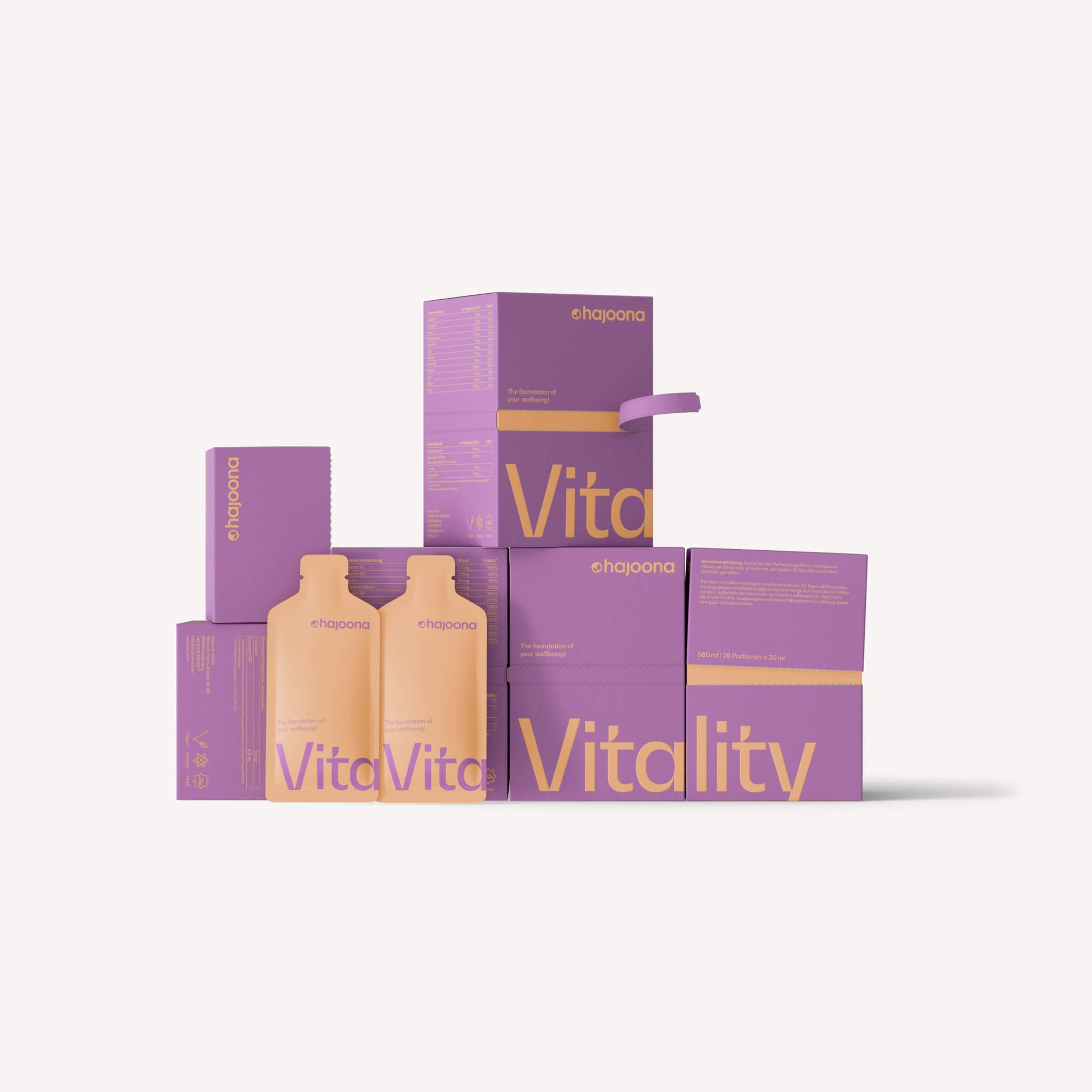 Produktabbildung von hajoona Vitality. Mehrere lilane Kartonverpackungen stehen nebeneinander und aufeinander gestapelt. Zwei peachfarbene Sachets lehnen an einer Verpackung.