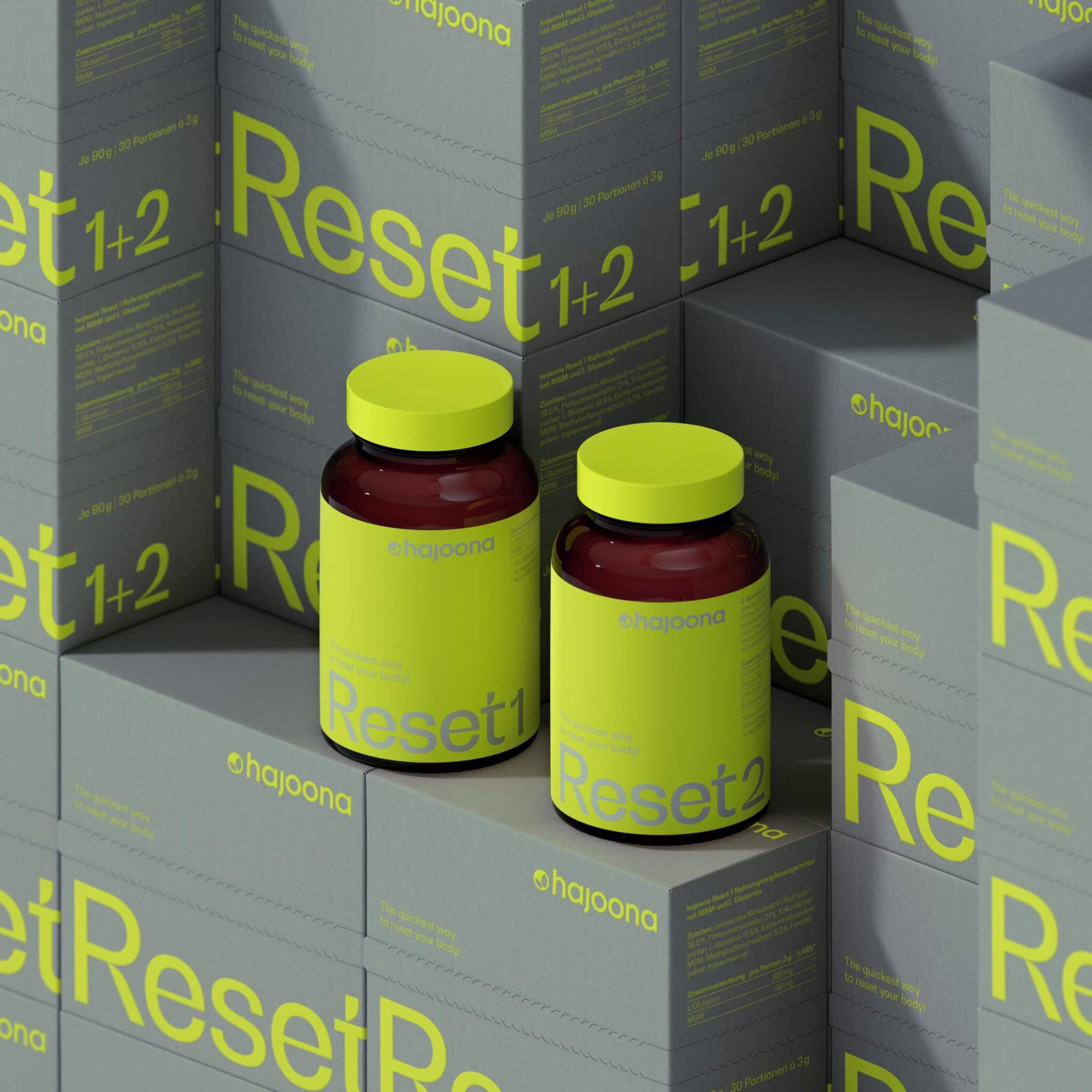 Zwei braune Glasbehälter mit neonfarbenem Etikett und Deckel, beschriftet mit "Reset 1" und "Reset 2" von hajoona. Die Flaschen stehen auf gestapelten Produktkartons mit der Aufschrift "Reset 1+2" in leuchtendem Grün auf grauem Hintergrund. Modernes, minimalistisches Verpackungsdesign.